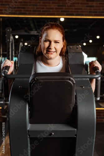 purposeful overweight girl doing arms extension exercise on fitness machine