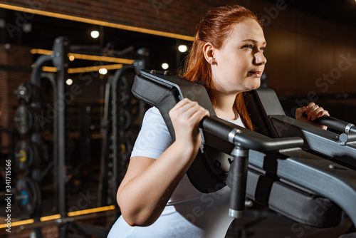 confident overweight girl doing arms extension exercise on fitness machine