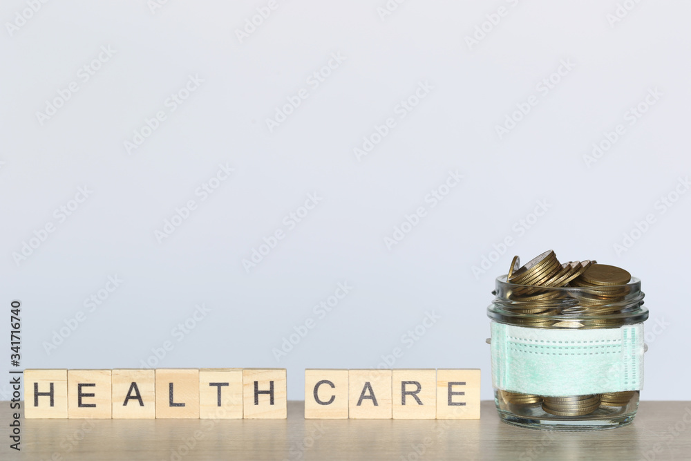 Stack of coins money in glass bottle with wearing protective medical mask on white background,Save money for Medical insurance and Health care concept Stack of coins money in glass bottle with wearing protective medical mask on white background,Save money for Medical insurance and Health care concept