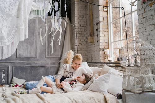 Mother and daughter hugging and cuddling in bed. Pretty little girl and beautiful woman with short haircut lie together in stylish bedroom. Family weekend, beauty day, having fun, love concept. © anna_gorbenko
