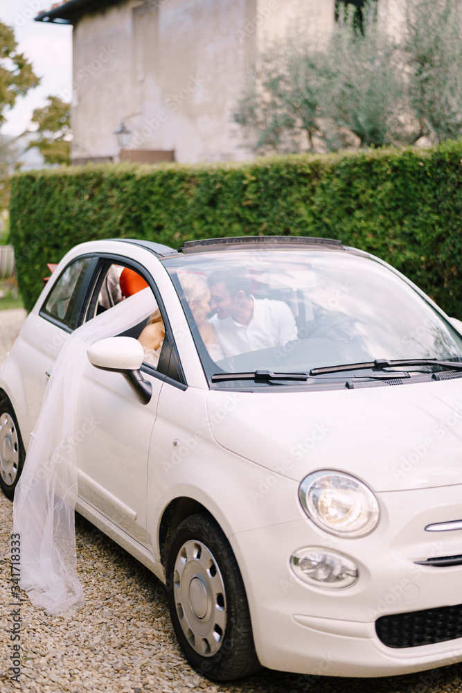 Beautiful bride and groom leaning forehead to forehead in a convertible in front of the Medici Villa of Lilliano Wine, Tuscany, Italy.