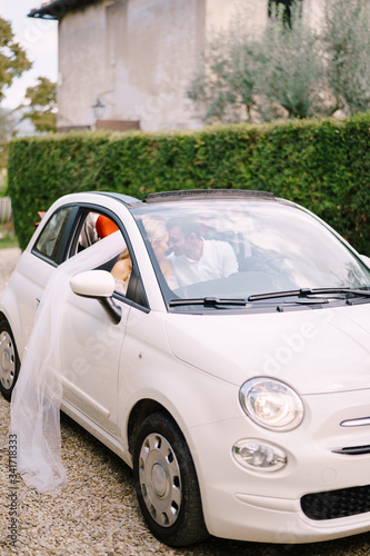 Beautiful bride and groom leaning forehead to forehead in a convertible in front of the Medici Villa of Lilliano Wine, Tuscany, Italy.