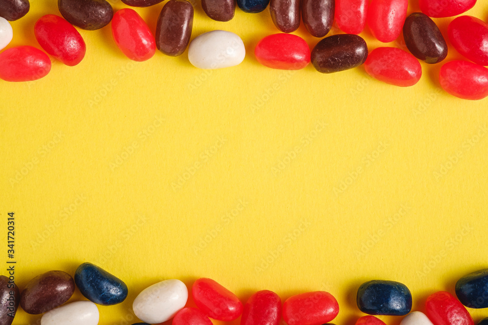 Frame of juicy sweet fruit colorful jelly beans on bright yellow background, top view copy space