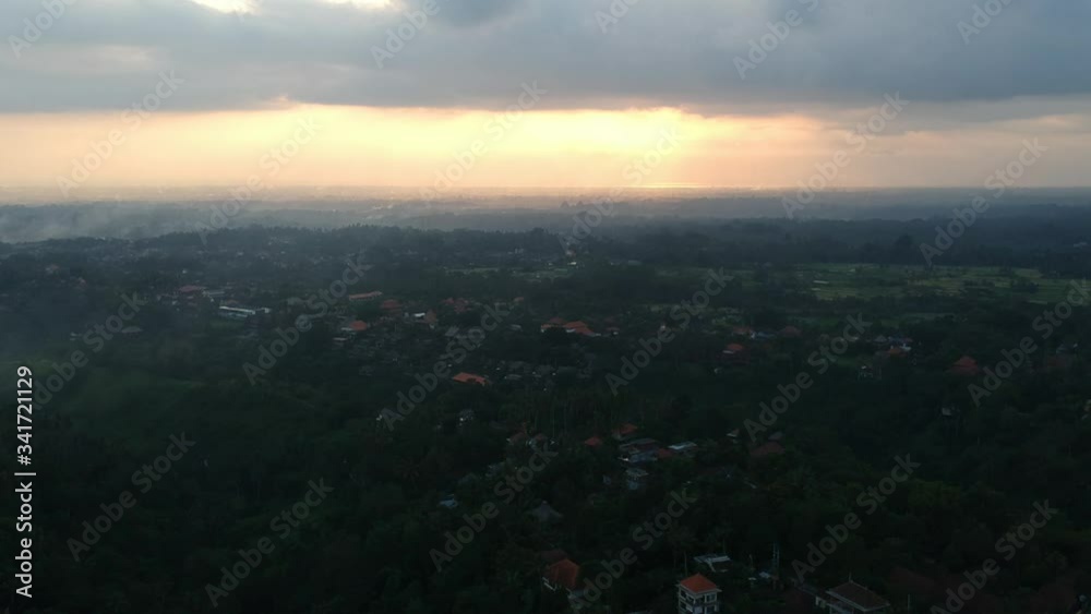 quadrocopter flies over the jungle of Ubud to a bali by sunset in the clouds, palm trees and houses with red roofs are visible. the weather is cloudy and gray, the whole sky is in the clouds and the quadrocopter flies over the jungle of Ubud to a bali by sunset in the clouds, palm trees and houses with red roofs are visible. the weather is cloudy and gray, the whole sky is in the clouds and the