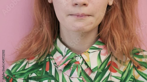closeup on red headed girl in flowered shirt showing her tongue with colorful letters on it. weird gonzo crazy portrait of laughing and smiling unrecognisable young female on pink background