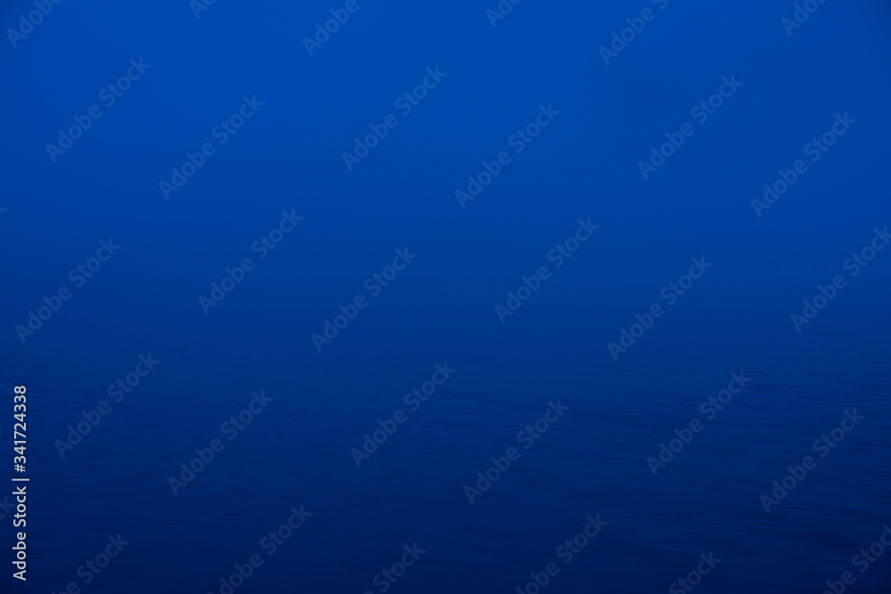 Obraz premium Natural texture of deep blue calm water in dusk close up. Night sea of blue classic color. Water ripple nature background. Meditative image of thick fog above lake. Soft light shines on water surface.