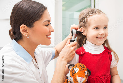 Audiologist examining little patient with otoscope, hearing exam of child