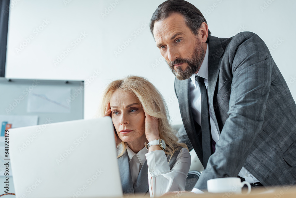 Selective focus of concentrated business people looking at laptop in office Selective focus of concentrated business people looking at laptop in office