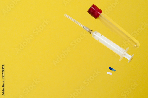 Flatlay, syringe, test tube and pills on a yellow background with place for text.
