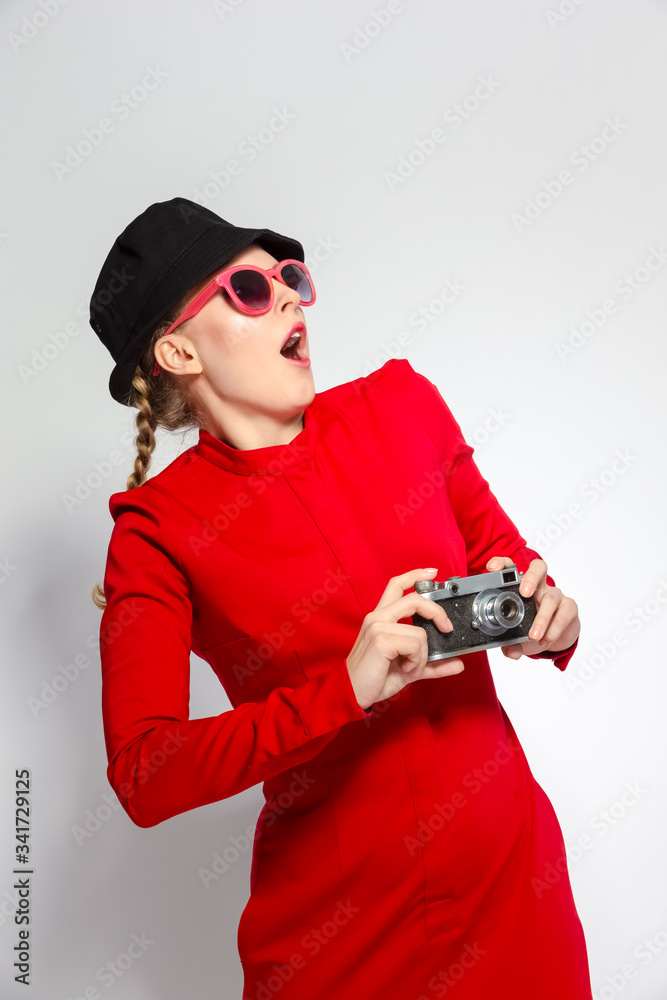 Surprised Caucasian Blond Girl With Old School Film Camera in Red Dress with Sunglasses. Taking Pictures Against White. Surprised Caucasian Blond Girl With Old School Film Camera in Red Dress with Sunglasses. Taking Pictures Against White.