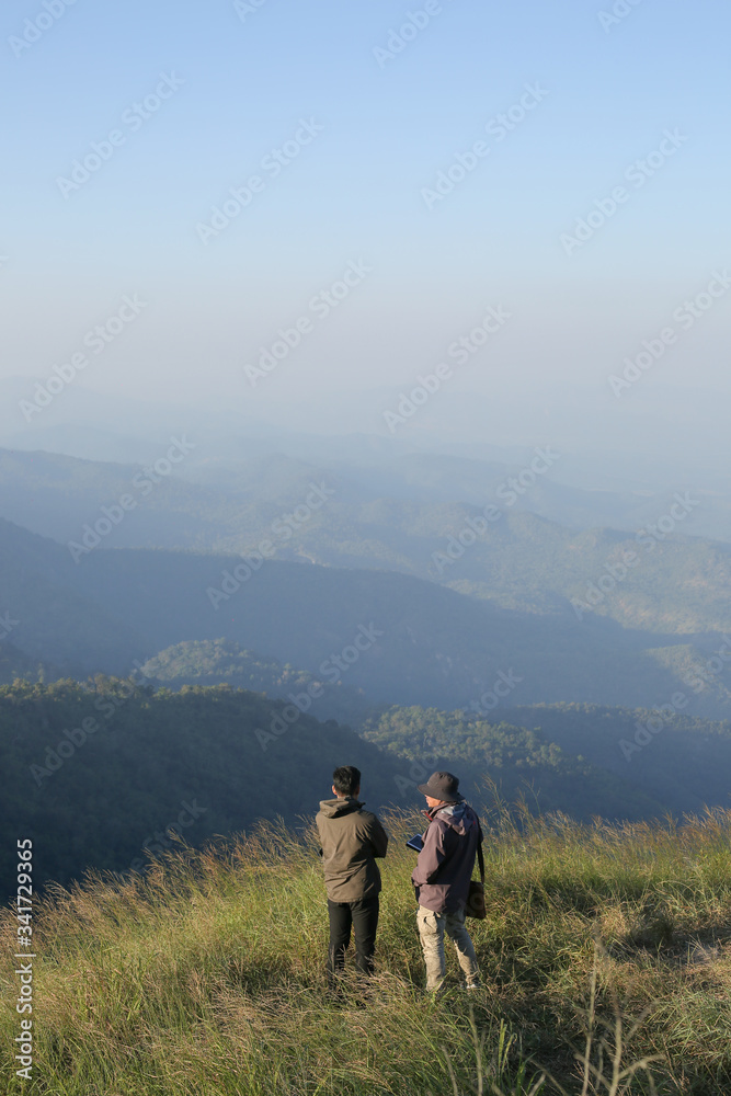 Two man have on jacket stand on hilltop look at beautiful mountain view
