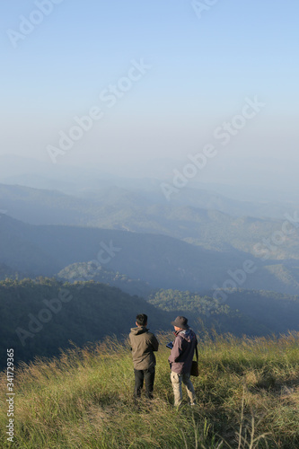 Two man have on jacket stand on hilltop look at beautiful mountain view