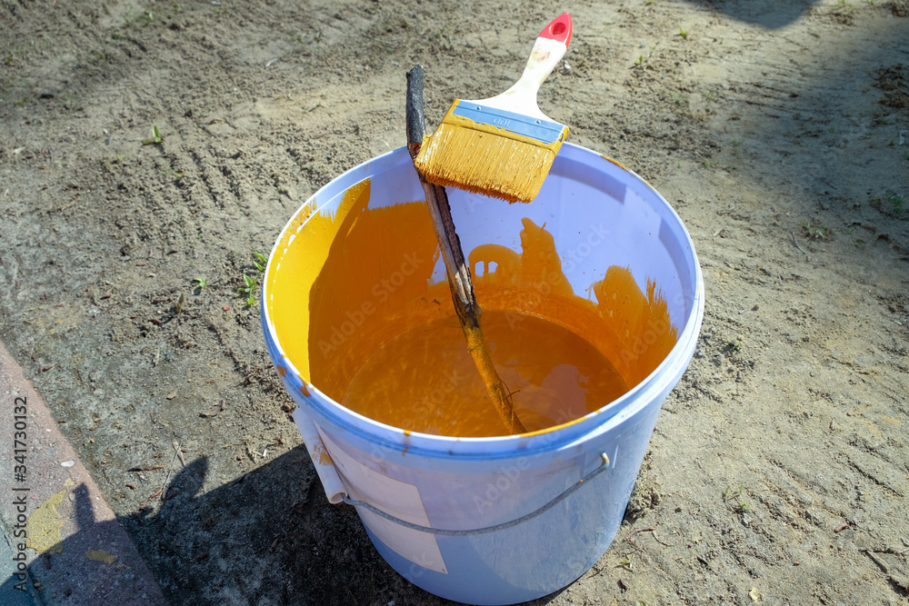 A bucket of yellow paint and a paintbrush A bucket of yellow paint and a paintbrush