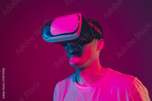 Playing with VR, shoting, driving. Caucasian man's portrait isolated on pink-purple studio background in neon light. Male model with devices. Concept of human emotions, facial expression, sales, ad. © master1305