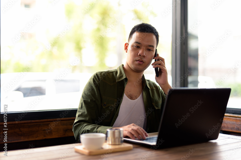 Young Asian man talking on the phone at the coffee shop Young Asian man talking on the phone at the coffee shop