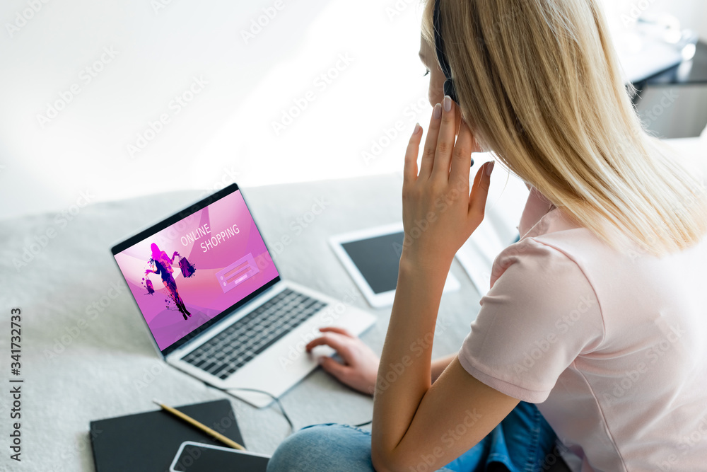 Fototapeta premium selective focus of freelancer touching headset near laptop with online shopping website and digital tablet with blank screen on bed