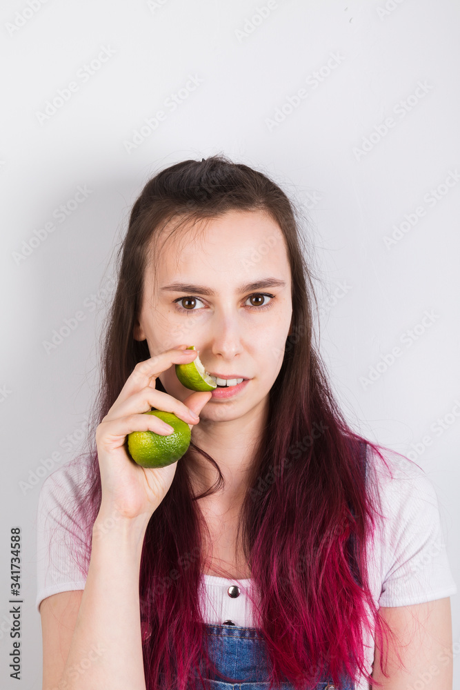Young girl with pink hair eats lime on grey background Young girl with pink hair eats lime on grey background