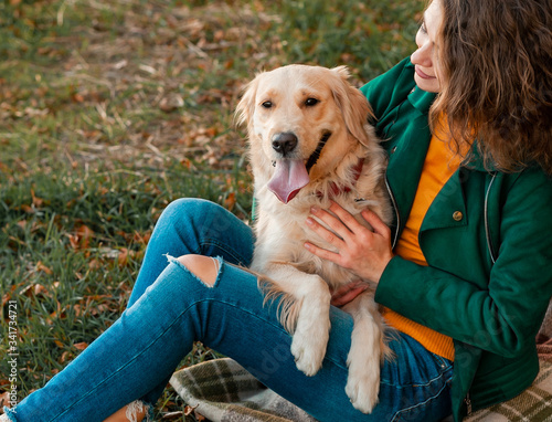 Smiling woman hugging her pet golden retriever dog near face. Golden retriever dog playing with a curly woman walking outdoors sunny day. love and care for the pet.