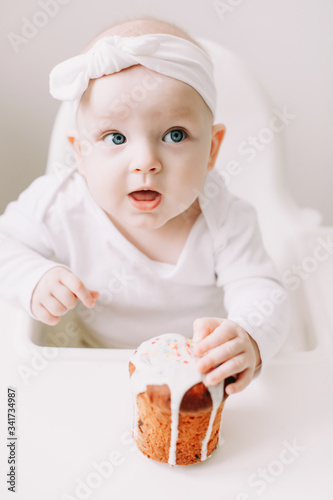 Cute baby in a baby chair eating the cake with his hands. Baby with a birthday cake on white background. Happy birthday concept photo