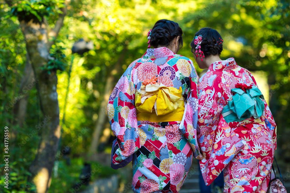 Japan Destination. Two Young Female Geishas in Traditional Japanese Floral Silk Kimono Going Uphill in Green Forest in Kyoto City, Japan. Japan Destination. Two Young Female Geishas in Traditional Japanese Floral Silk Kimono Going Uphill in Green Forest in Kyoto City, Japan.