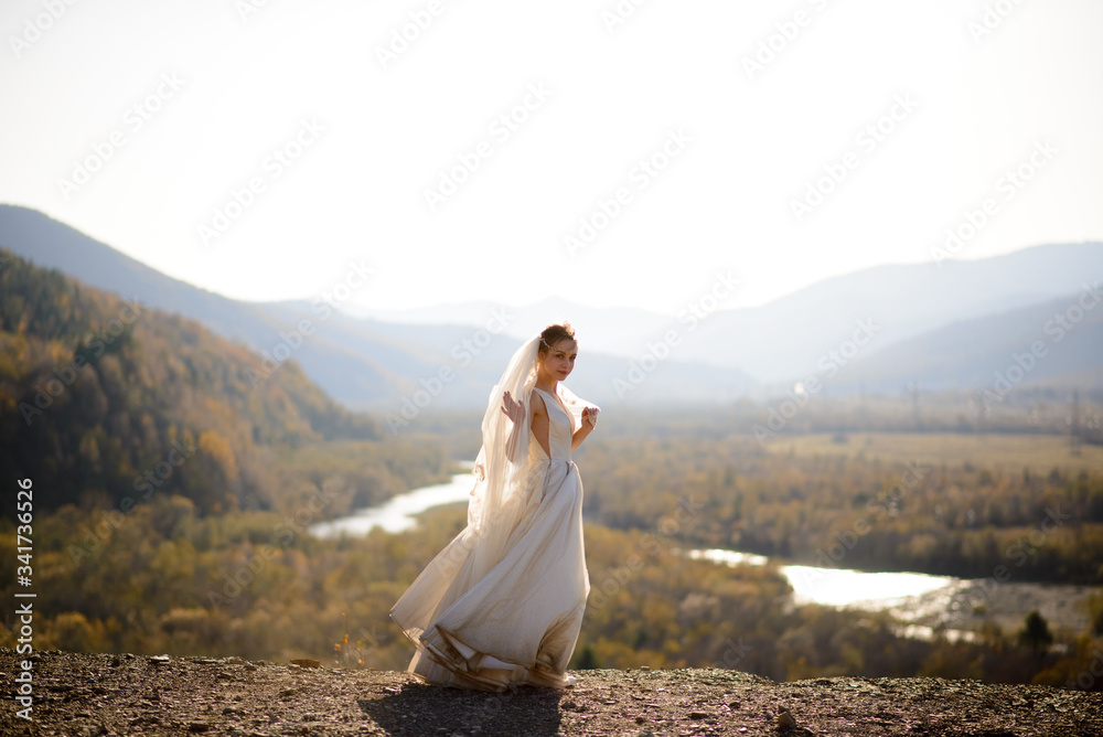 Portrait of a young beautiful bride in the mountains with a veil. The wind develops a veil. Wedding photography in the mountains.