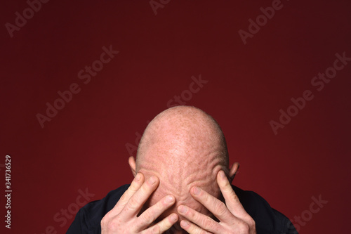 bald man touching his head with wrinkles on red background