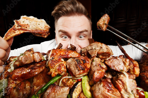 Crazy hungry man eating mix grill meat. Emotional content for restaurant promo. Cheat day. Meat lover. Lamb chops, chicken tikka, kebab, lamb, beef steak. Enjoy your food