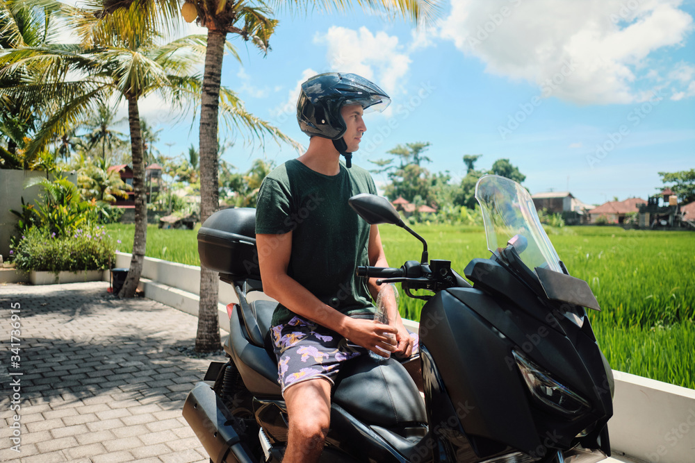 Young man in helmet riding on scooter through beautiful tropical island