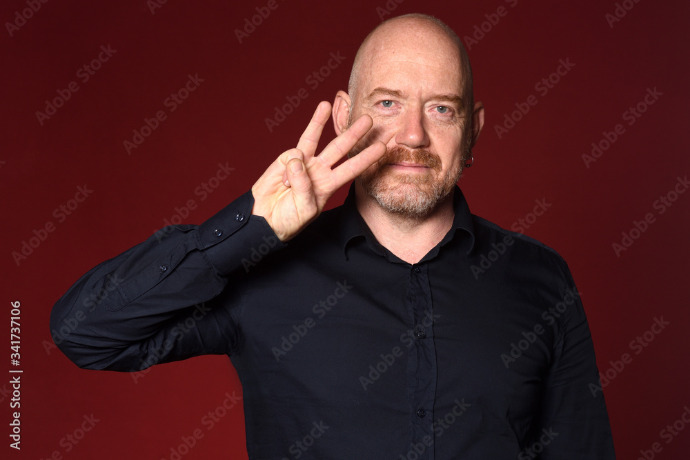 portrait of a man with fingers making number three on red background portrait of a man with fingers making number three on red background