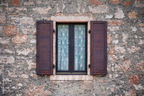 Italian window on the stone wall facade with open wooden brown color classic shutters
