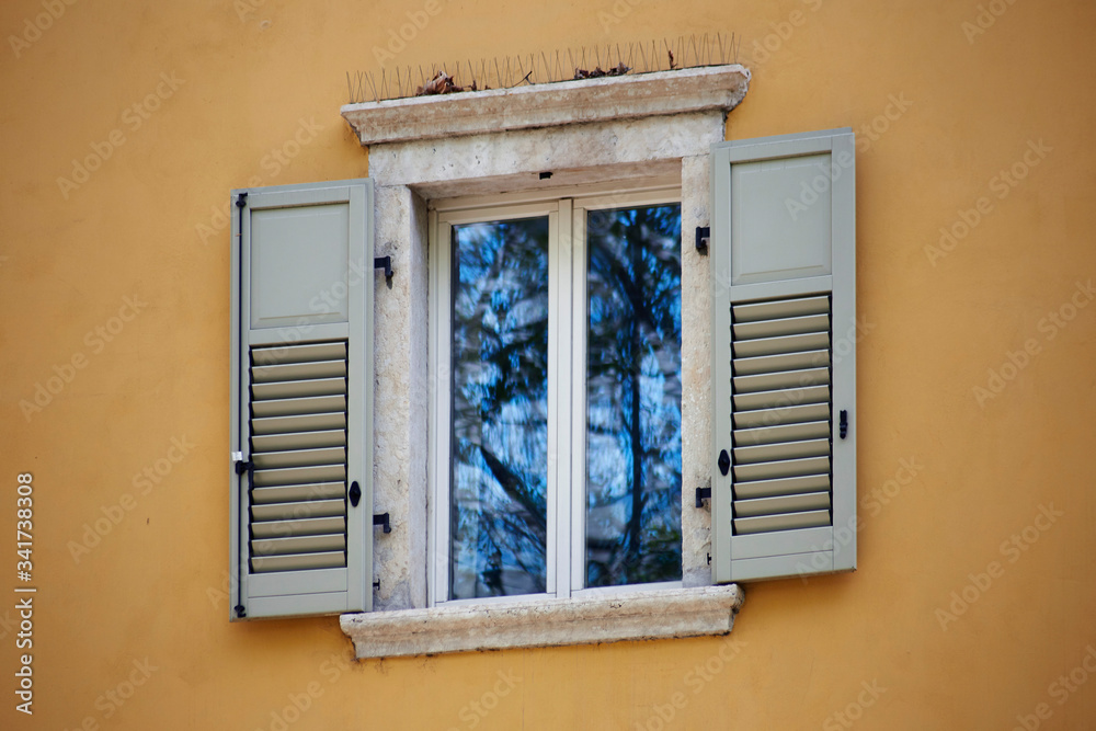 Italian window on the yellow wall facade with open wooden light grey color classic shutters