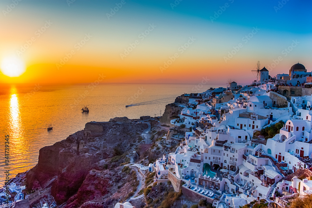 Fototapeta premium Greek Traveling Concepts. Sailing Boats Near Caldera Volcanic Slopes of Santorini Oia or Ia Village in Greece Enjoying Sunset.