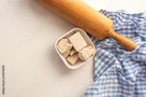 close up detail of fresh yeast cube  on a white background in a white porcelain dish with rollingpin  