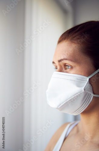 Young woman looking out of window wearing protective face mask.