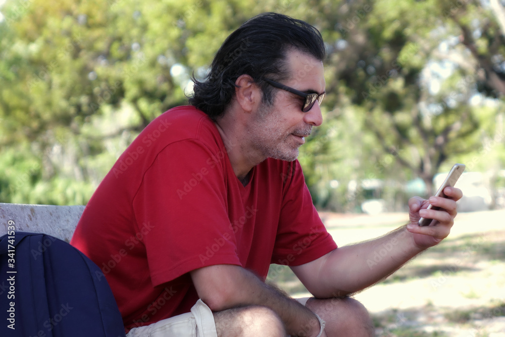 Outdoor portrait of a mid adult man sitting on park bench using mobil phone in Florida, USA