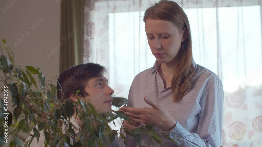 Happy young couple hugging and kissing in bright room decorated with houseplants near the window Happy young couple hugging and kissing in bright room decorated with houseplants near the window