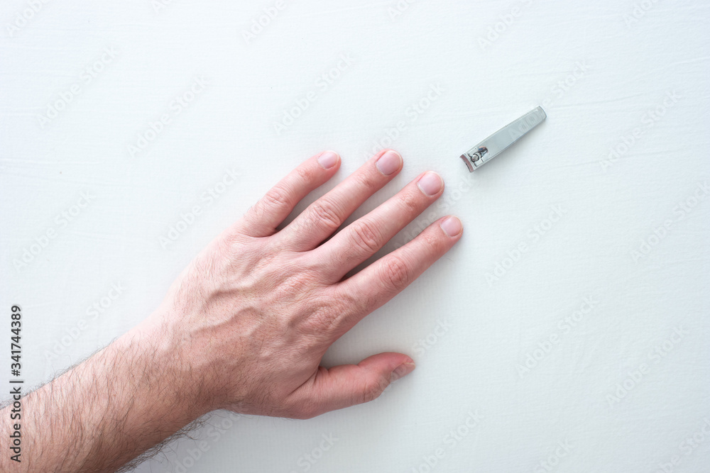 Caucasian male straight extended hand and uncut long nails and nail clipper on white surface top view close up shot Caucasian male straight extended hand and uncut long nails and nail clipper on white surface top view close up shot