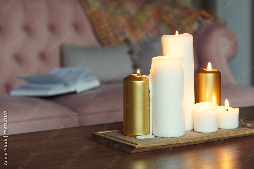 Lightened candles on a wooden table and an open book lying on a sofa in the background Lightened candles on a wooden table and an open book lying on a sofa in the background