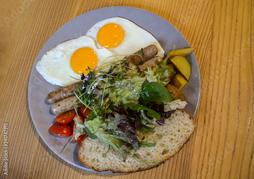 Plate of fried eggs and fried sausages with fresh salad, potatoes and bread for breakfast