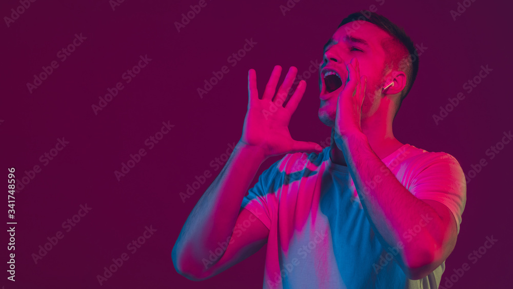 Calling, shouting. Caucasian man's portrait isolated on pink-purple studio background in neon light. Beautiful male model with earphones. Concept of human emotions, facial expression, sales, ad. Calling, shouting. Caucasian man's portrait isolated on pink-purple studio background in neon light. Beautiful male model with earphones. Concept of human emotions, facial expression, sales, ad.