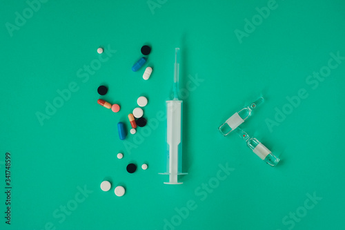 syringe and multicolored pills on green background