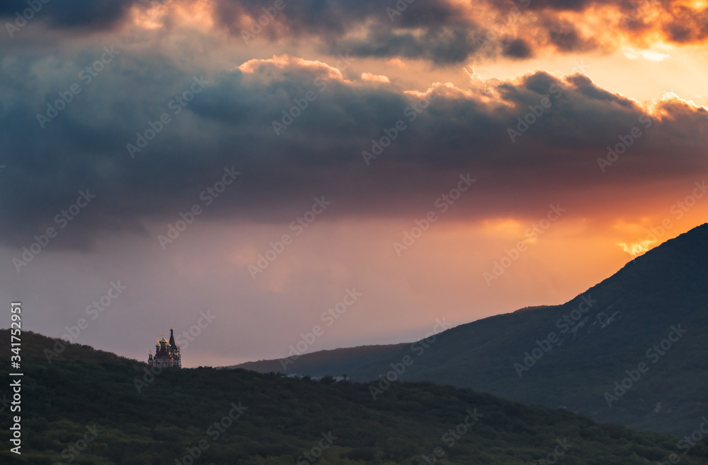 Small church in the mountains and beautiful gray clouds at sunset