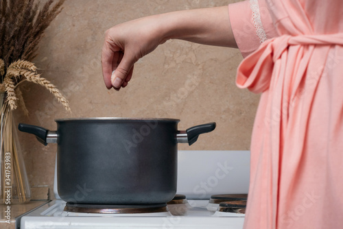 Woman is cooking a food in the casserole on the stove close up.