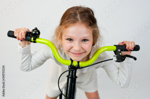Beautiful little girl with curly hair in a light dress on a new bright bicycle. Shot on a light background.