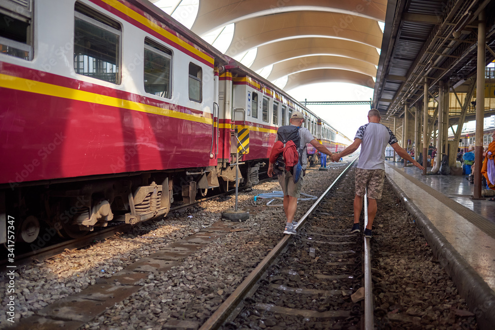 Obraz premium Bangkok, Thailand - January 2020: Rear view of a gay tourist couple on the train tracks at a railway station in Thailand