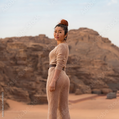 Beautiful Asian girl in a translucent flesh-colored long dress and mouth-watering forms stand on a rock against the backdrop of rocks