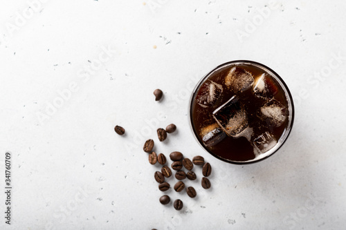 ice coffee with ice cubes in a glass on a light background, coffee beans are scattered nearby