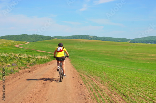 Young woman on bike, cyclist in field with green grass and yellow flowers, beautiful nature landscape, copy space