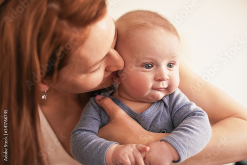 Woman holding her baby son on hands, kissing him on cheeks, closeup detail