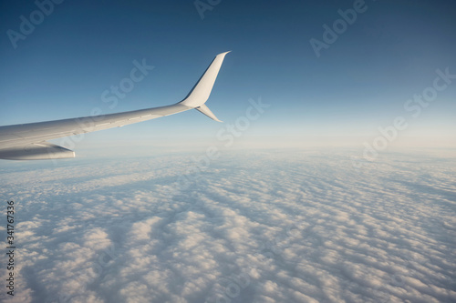 Wing of plane flying over cloudy in the blue sky